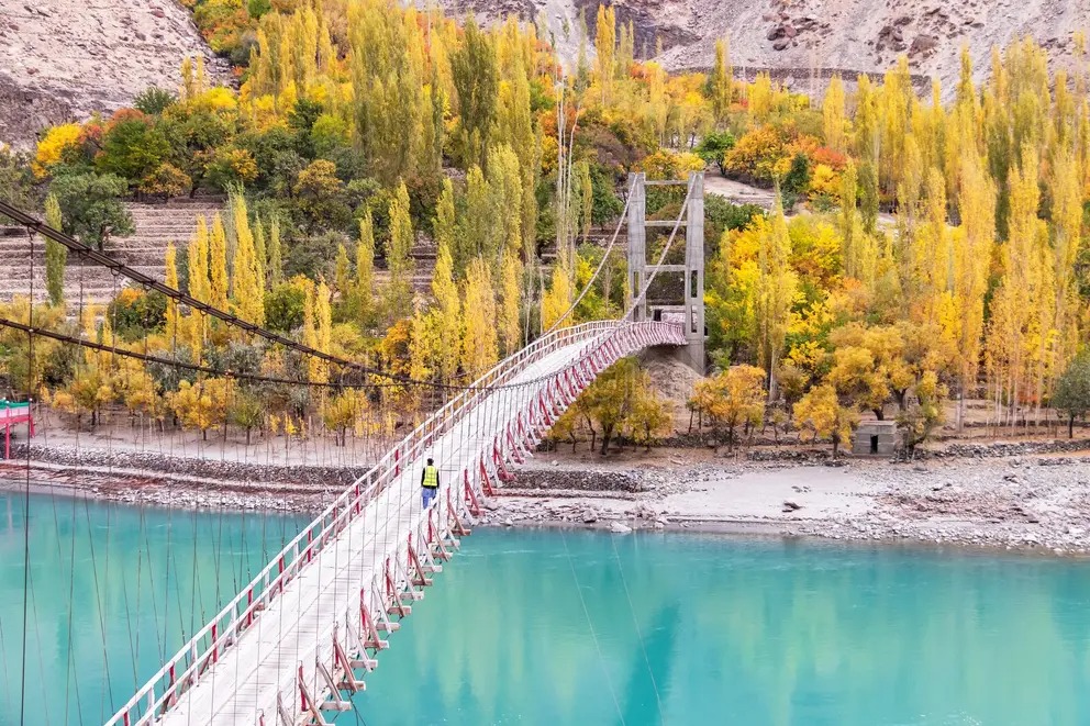 Autumn trees beside a suspension bridge in northern Pakistan